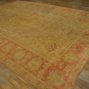 Faded gold and coral traditional area rug displayed on distressed wood plank flooring.