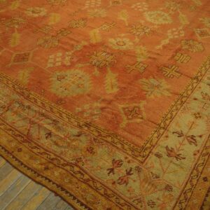 Angled view of a low-pile rug with an orange field and yellow-tan stylized floral borders.