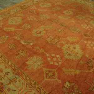 A large, terracotta rug with faded gold and green traditional motifs lies on gray wooden floors.