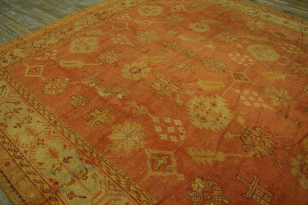 A large, terracotta rug with faded gold and green traditional motifs lies on gray wooden floors.