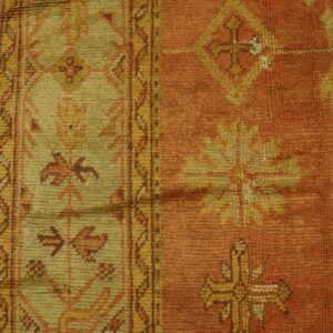 Geometric patterned rug in rust and yellow-green with a medium pile lies against a cracked yellow surface.