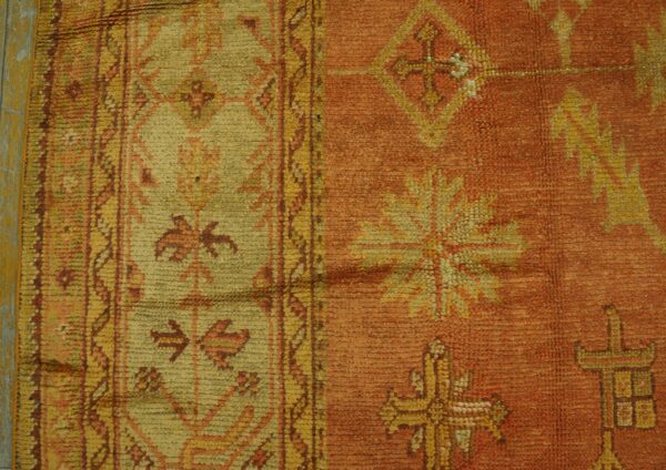 Geometric patterned rug in rust and yellow-green with a medium pile lies against a cracked yellow surface.