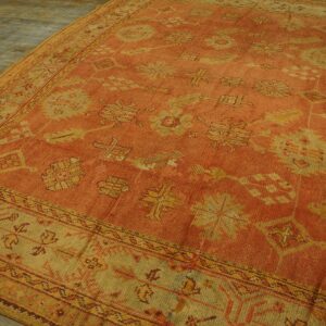 A low-pile orange rug displays stylized yellow motifs and detailed borders over rustic wood floors.
