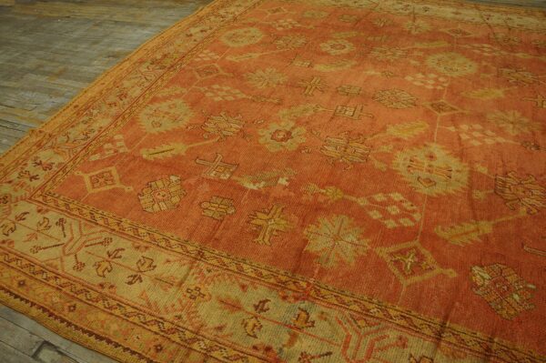 A low-pile orange rug displays stylized yellow motifs and detailed borders over rustic wood floors.