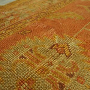 Highly textured orange and gold rug detail shows abstract patterns against blurred light flooring.