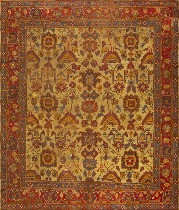 Low-pile rug featuring a complex geometric design in faded gold, deep red, blue, and dark brown colors.