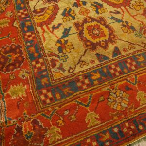 Textured rug in gold, red, and teal with detailed central motifs and complex borders on wood floor.