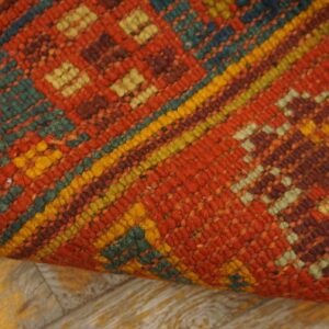 Textured, low-pile rug in terracotta, teal, and yellow geometric patterns, resting on light wood floorboards.