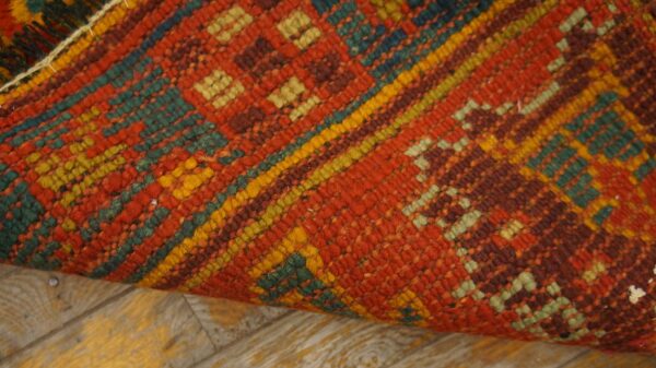 Textured, low-pile rug in terracotta, teal, and yellow geometric patterns, resting on light wood floorboards.