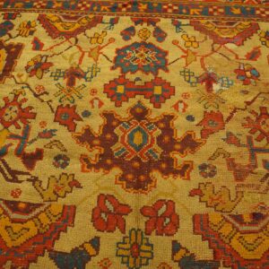 Textured rug detail with angular tribal motifs in gold, rust, and teal on a bright yellow field.