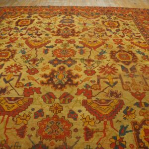Gold rug with red, yellow, and blue geometric and stylized traditional motifs on wood floor.
