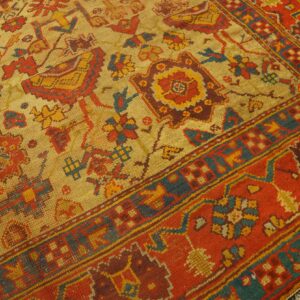 Low-pile rug with a gold field, stylized red and teal motifs, and a thick, vibrant red border.