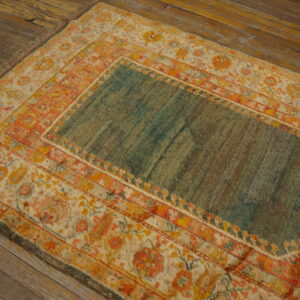 Teal and orange patterned rug with low pile on rustic brown wood plank flooring.