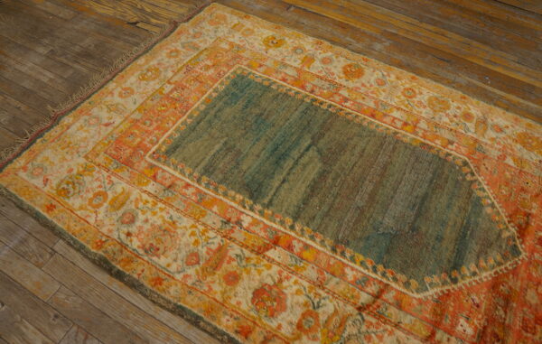 Teal and orange patterned rug with low pile on rustic brown wood plank flooring.