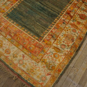 A teal rug with distressed orange and cream floral borders rests on rustic light wood plank flooring.