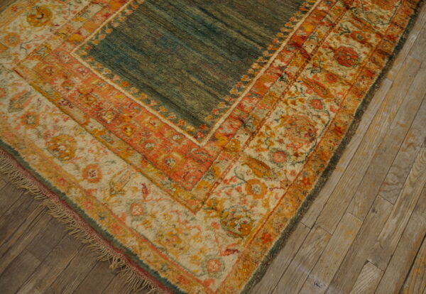 A teal rug with distressed orange and cream floral borders rests on rustic light wood plank flooring.