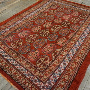 Red rug featuring repetitive geometric blue, pink, and tan medallions rests on rustic gray wood flooring.