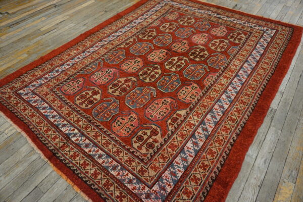 Red rug featuring repetitive geometric blue, pink, and tan medallions rests on rustic gray wood flooring.
