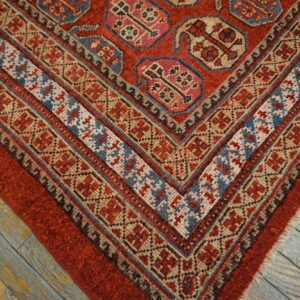 Geometric red rug with complex patterned borders rests on wide distressed gray wood planks.