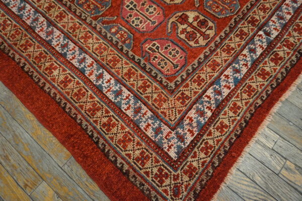 Geometric red rug with complex patterned borders rests on wide distressed gray wood planks.