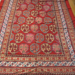 A deep red rug with geometric blue, tan, and pink motifs rests on light wood planks.