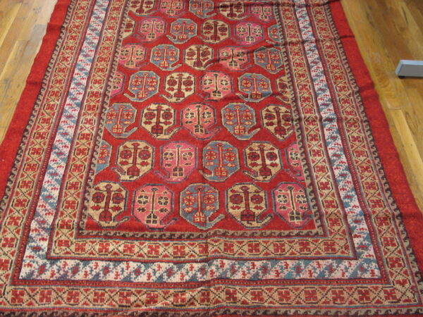 A deep red rug with geometric blue, tan, and pink motifs rests on light wood planks.