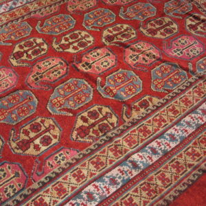 Red medium-pile rug displaying repeating stylized motifs in blue, pink, and cream with striped borders.