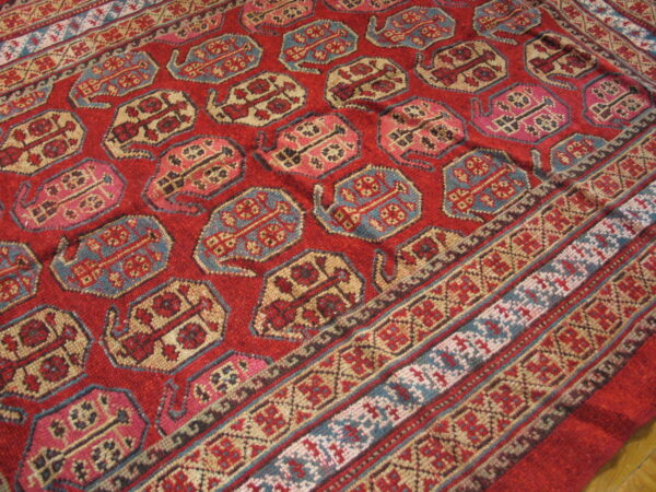 Red medium-pile rug displaying repeating stylized motifs in blue, pink, and cream with striped borders.