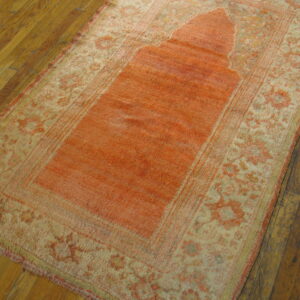 Low-pile rug in bright coral and beige with a central niche pattern on dark wood plank flooring.