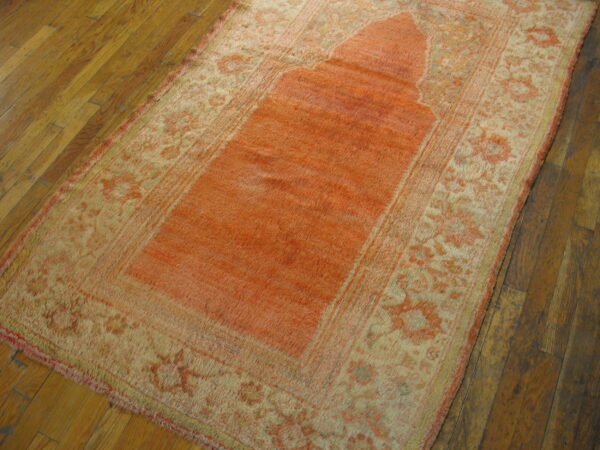 Low-pile rug in bright coral and beige with a central niche pattern on dark wood plank flooring.