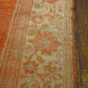 Faded orange and cream high-pile rug with a floral pattern rests on dark wooden plank flooring.