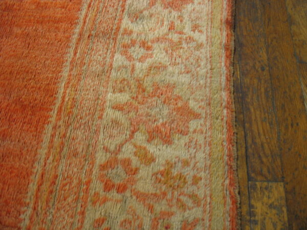 Faded orange and cream high-pile rug with a floral pattern rests on dark wooden plank flooring.
