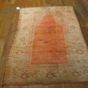 Rectangular orange and beige patterned rug featuring a niche design rests on distressed wooden floors.