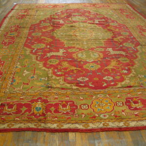 Ornate red and olive green rug features animal patterns, a central medallion, and detailed borders on wood planks.