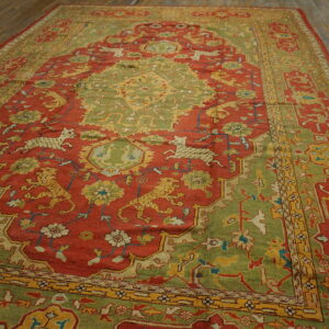 Earthy red and moss green traditional rug featuring complex animal figures and yellow accents on wood planks.