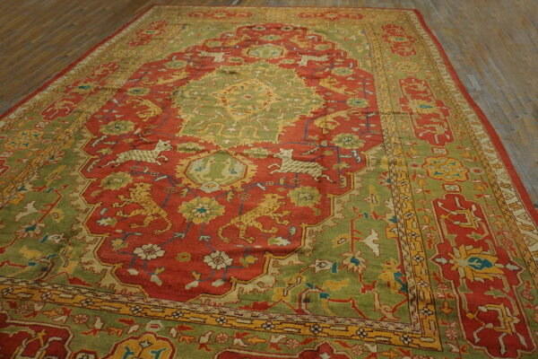 Earthy red and moss green traditional rug featuring complex animal figures and yellow accents on wood planks.