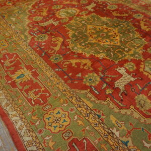 A traditional red and green rug featuring stylized animal motifs rests on light gray distressed wood flooring.