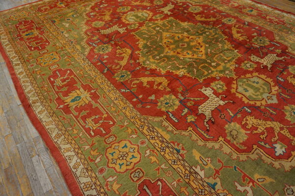 A traditional red and green rug featuring stylized animal motifs rests on light gray distressed wood flooring.