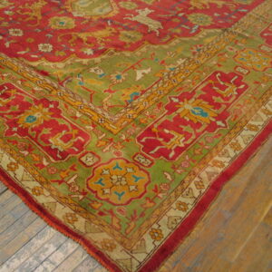 Ornate red, green, and gold patterned rug corner resting on weathered wood plank flooring.