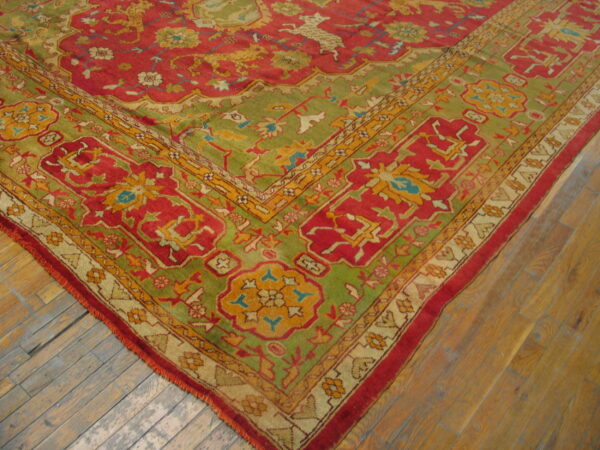 Ornate red, green, and gold patterned rug corner resting on weathered wood plank flooring.