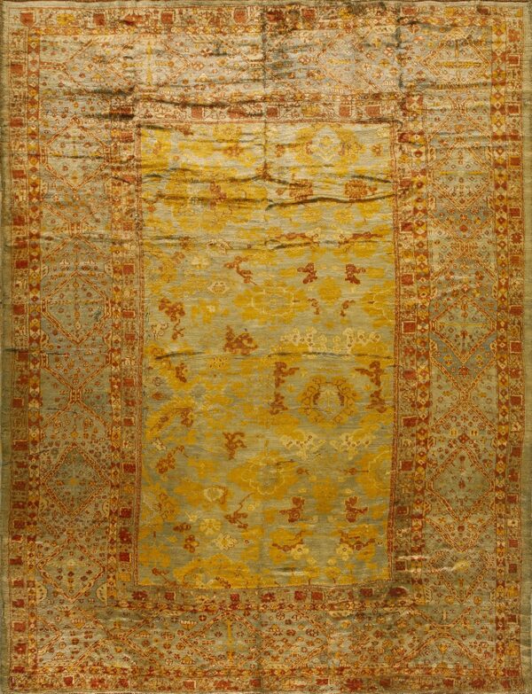 Ornate yellow, rust, and blue-green rug displaying heavy sheen and a complex bordered medallion design.