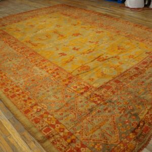 Oversized rug with faded yellow, red, and sage green traditional patterns displayed on plank wood flooring.