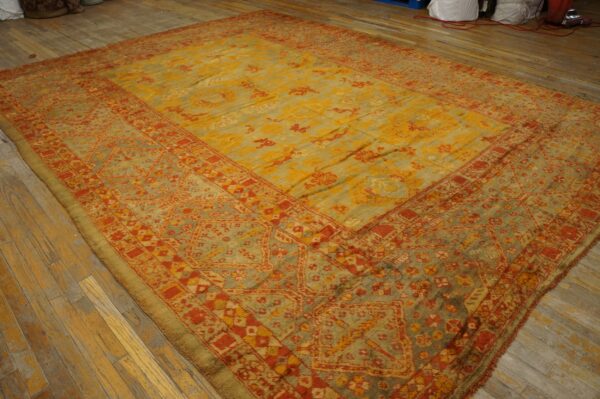 Oversized rug with faded yellow, red, and sage green traditional patterns displayed on plank wood flooring.