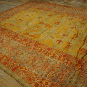 Distressed traditional rug in yellow, sage, and red patterns lies on rustic wooden floorboards.