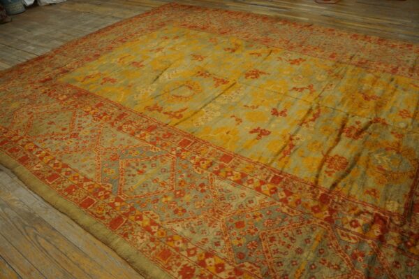 Distressed traditional rug in yellow, sage, and red patterns lies on rustic wooden floorboards.