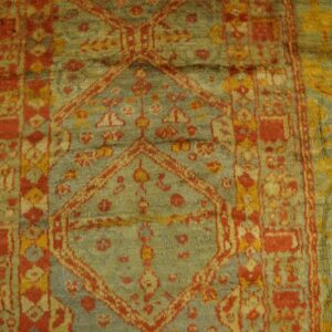 Geometric patterned rug with red, gold, and faded blue-green pile lies partially on distressed wood floor.