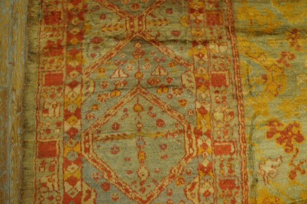 Geometric patterned rug with red, gold, and faded blue-green pile lies partially on distressed wood floor.