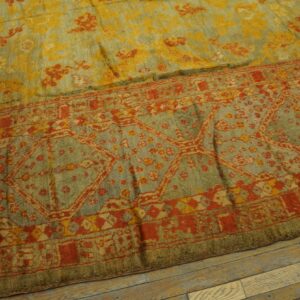 Distressed blue-green rug with rust red borders and yellow floral patterns on wood flooring.