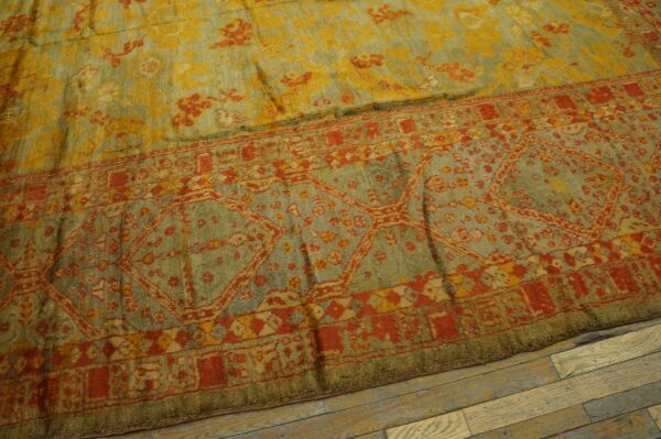 Distressed blue-green rug with rust red borders and yellow floral patterns on wood flooring.