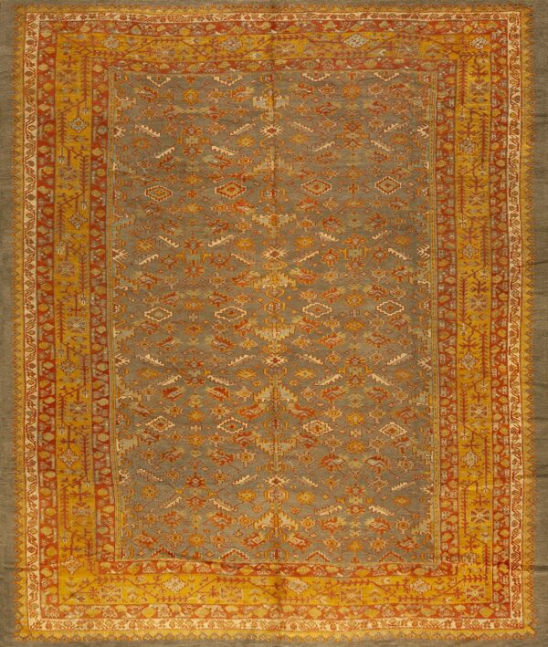 Muted gray rug featuring geometric tribal motifs and wide borders in gold and rust red.